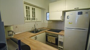 A compact kitchen with white cabinets, a stainless steel refrigerator, a built-in oven, and a sink. - Seven Seconds Away (Athens)
