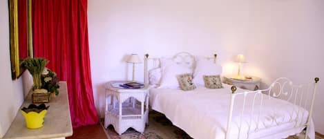 A bedroom with a white bed, two bedside tables, a red curtain, and a floral carpet.