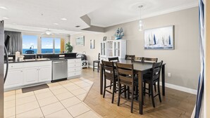 A modern kitchen with a dining area, large windows, and a view of the sea.