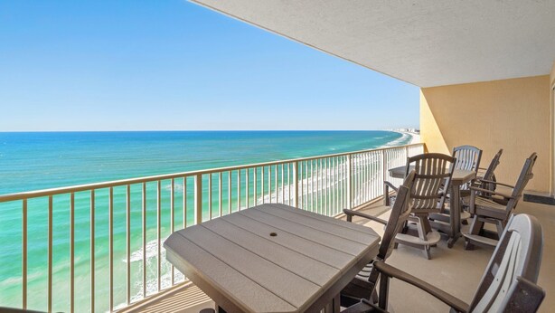 A balcony with a view of the ocean, a table, and several chairs.