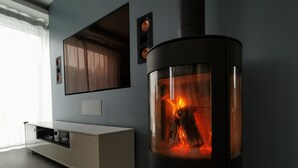 Una sala de estar moderna con un estufa de leña empotrada, un mueble de entretenimiento blanco y un amplio ventanal con cortinas traslúcidas.