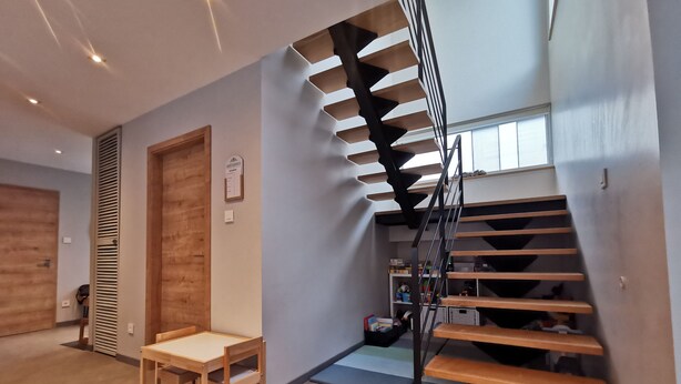 Un interior moderno con una escalera de madera, una mesita con una silla y una puerta con un respiradero.