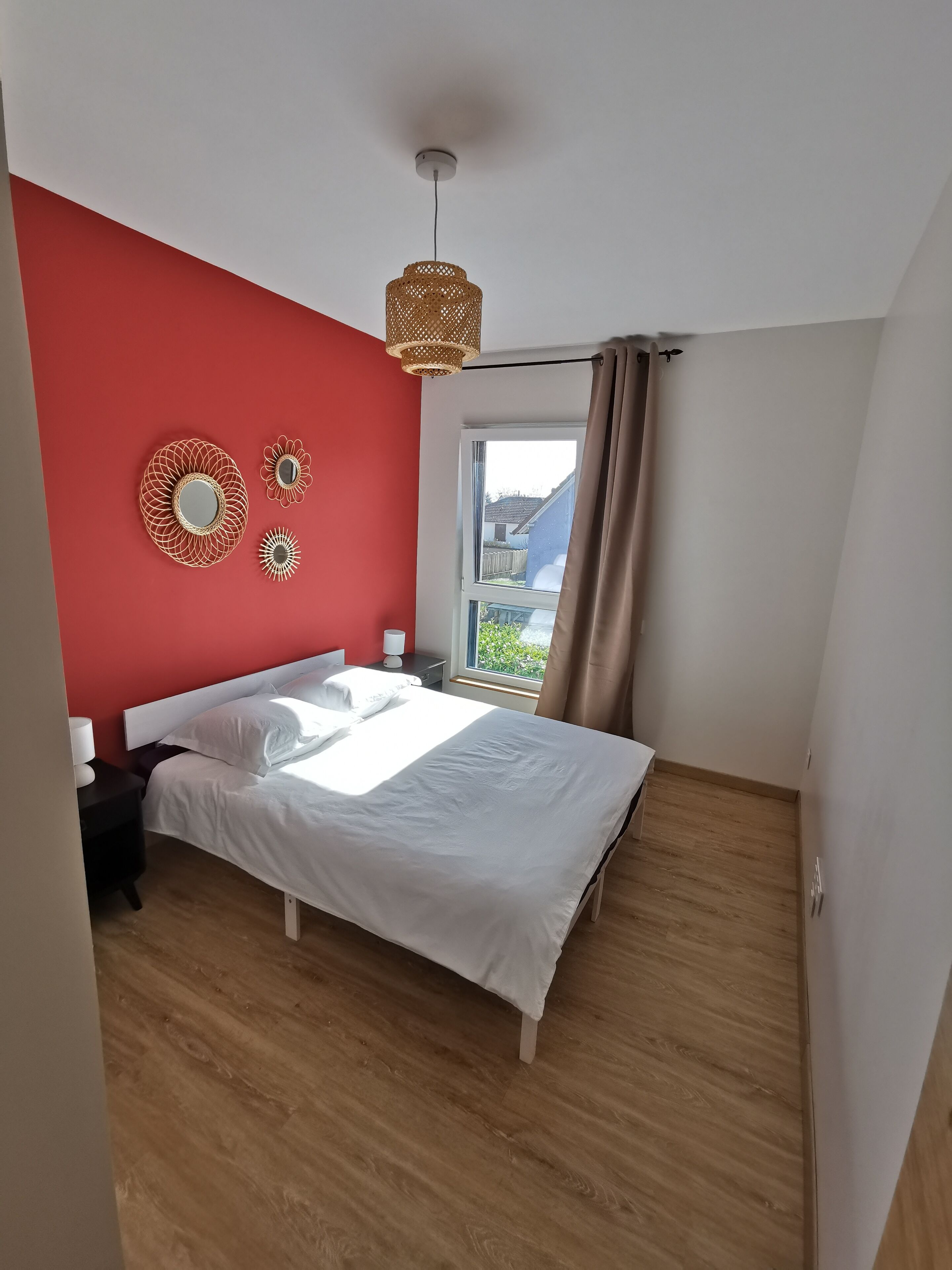 Ein Schlafzimmer mit Bett, Nachttisch, Nachttischlampe, einem Fenster mit Vorhängen und einer Pendelleuchte.