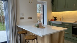 Une cuisine moderne dotée d’un îlot central, de tabourets de bar, de meubles de couleur verte et offrant une vue sur l’extérieur.