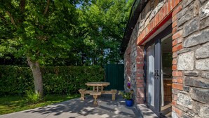 Une terrasse avec une table et des bancs en bois, un mur en pierre et une clôture verte.