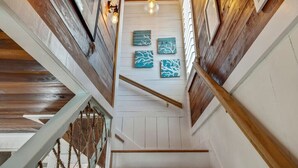 A staircase with wooden railings and a white wall with four blue artwork pieces. - A Rare Nautical Historic Gem! Steps to the Ocean! Grocery Next Door! (Panama City Beach)