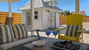 A covered outdoor seating area with a wooden table, a yellow chair, and a white building in the background. - A Rare Nautical Historic Gem! Steps to the Ocean! Grocery Next Door! (Panama City Beach)
