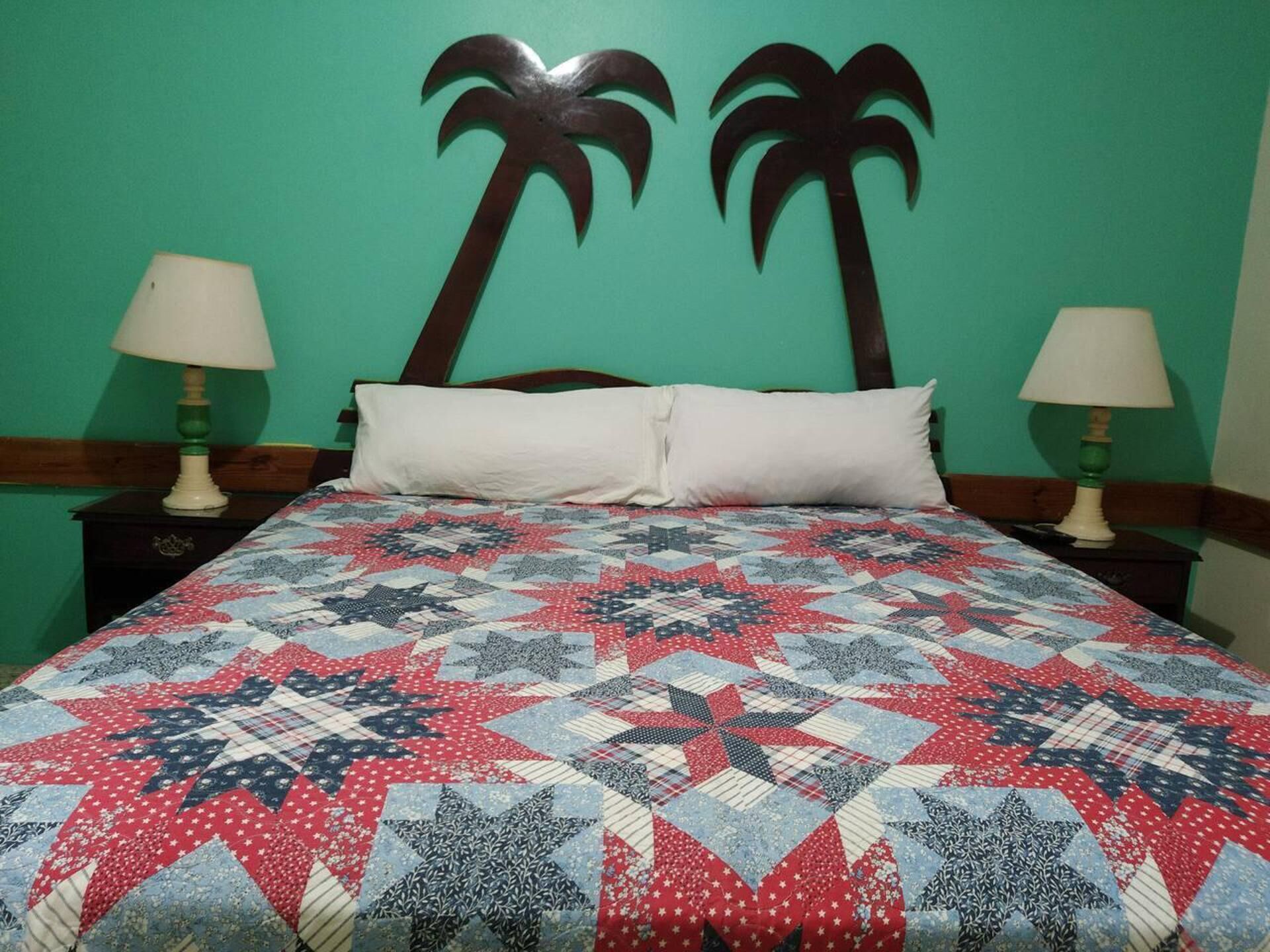 A bed with a star-patterned quilt, two nightstands with lamps, and a wall with two palm tree decorations.