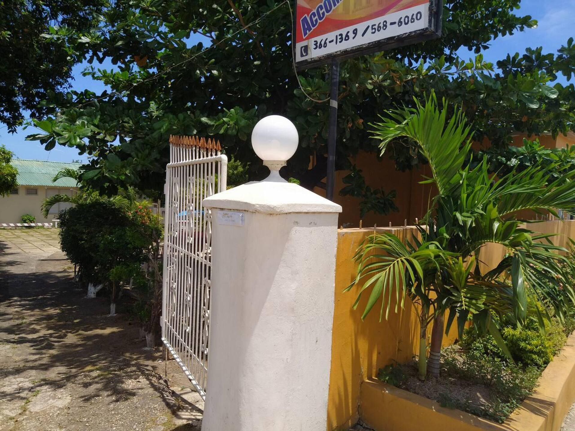 Ingresso recintato con un ornamento sferico bianco, un muro giallo e una targa con i numeri di contatto.