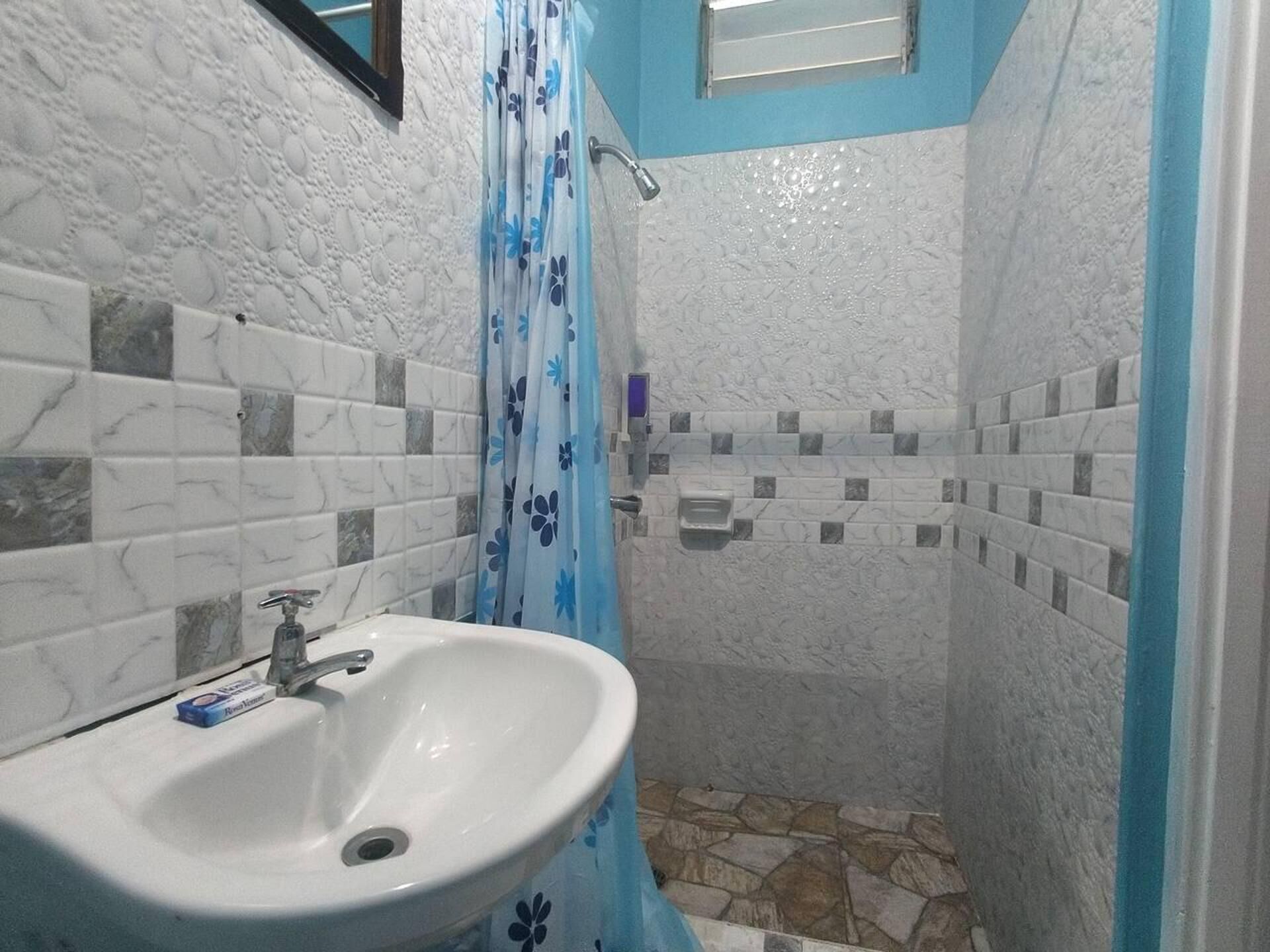 A bathroom with a white sink, a shower with a blue floral shower curtain, and tiled walls with a marble pattern.