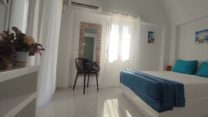 A bedroom with a bed, a chair, a window with curtains, and a wall with a picture. - JB VILLA ,Stunning Santorini Escape w/heated jacuzzi and enclosed garden. (SANTORINI AIGEAN GREECE)