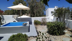 A rooftop pool area with a blue pool, a white umbrella, and surrounding greenery. - JB VILLA ,Stunning Santorini Escape w/heated jacuzzi and enclosed garden. (SANTORINI AIGEAN GREECE)