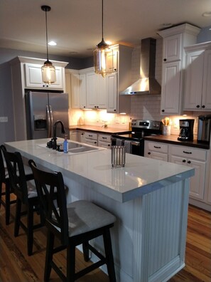 A modern kitchen with white cabinets, a large island with bar stools, stainless steel appliances, and pendant lighting.