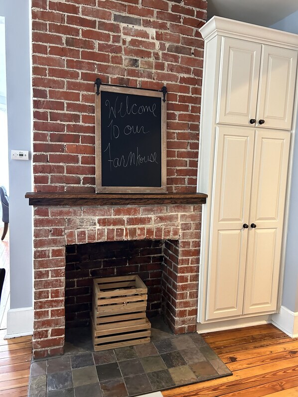 A brick fireplace with a welcome sign, wooden logs, and white cabinets.