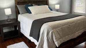 A bedroom with a wooden headboard, white bedding, a grey quilted throw, and a bedside table with a lamp. - Country Comfort and Views - 10 minutes from restaurants. (Newburgh)