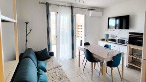 En moderne stue med en hjørnesofa, et spisebord med stole, et tv på væggen og et køkken med hårde hvidevarer.