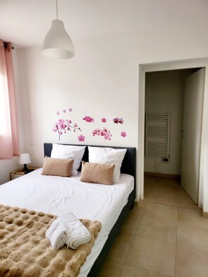 Un lit bien fait, avec une couverture moelleuse et des serviettes pliées, une lampe de chevet et une décoration florale fixée au mur.