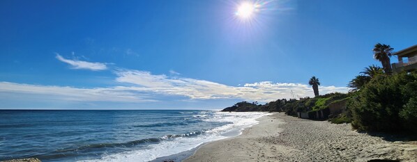 Une plage avec un ciel dégagé, une mer calme et un bâtiment doté d’un balcon donnant sur l’océan.