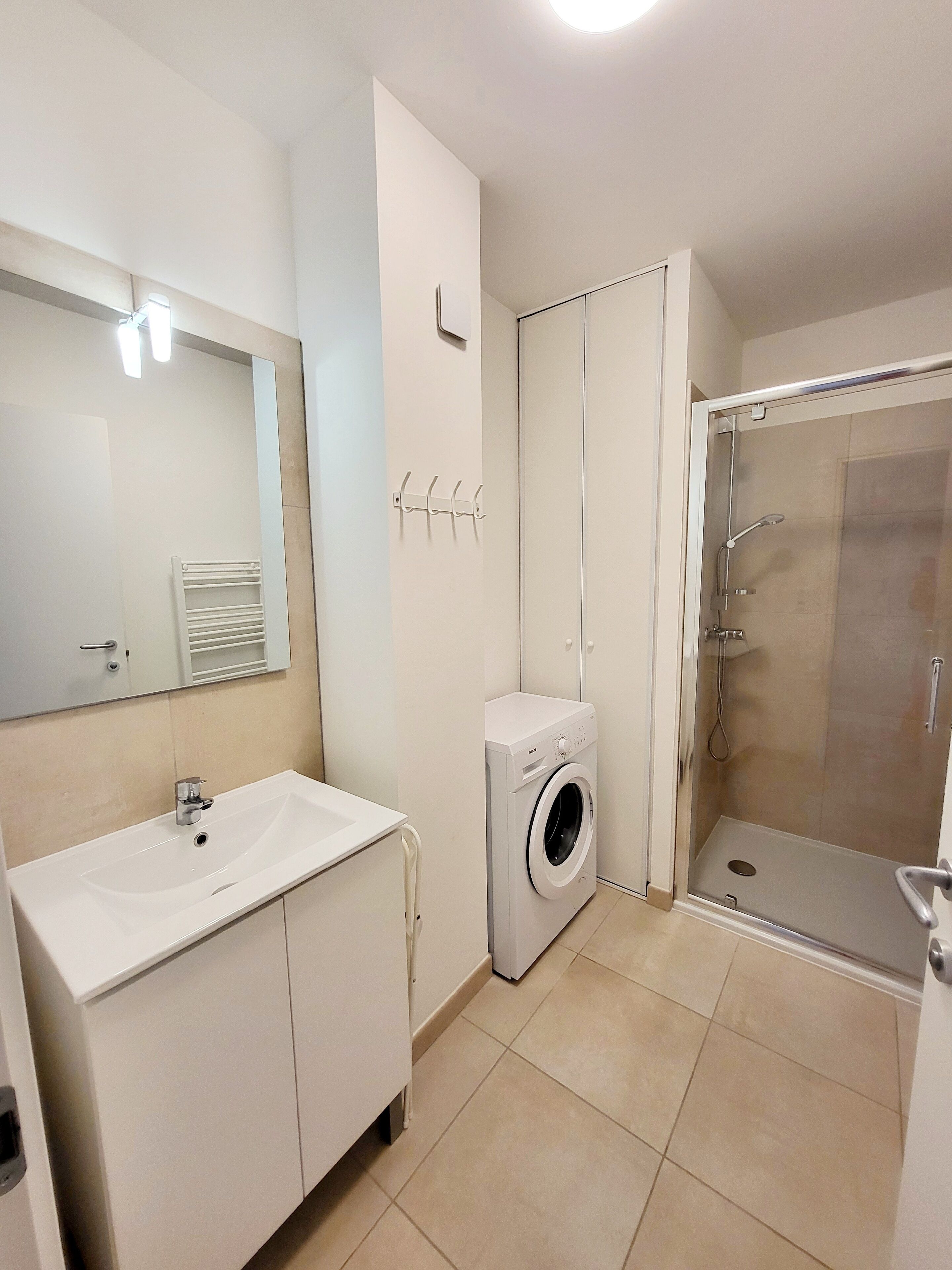 Un baño moderno con lavabo, espejo, lavadora y ducha con mampara de vidrio.