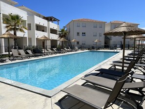Une piscine entourée de bâtiments à plusieurs étages dotés de balcons, avec des chaises longues et des parasols à proximité.