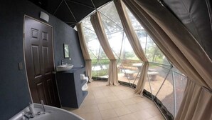 A modern bathroom with a bathtub, sink, and mirror. It features large windows with curtains, offering views of the outdoors. - Geodesic Dome 01, Jacuzzi with Hydromassage, 20 min from La Fortuna (Provincia de Alajuela)