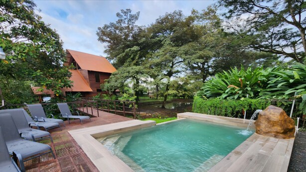 A pool area with a wooden deck, lounge chairs, and a stone feature. - Geodesic Dome 01, Jacuzzi with Hydromassage, 20 min from La Fortuna (Provincia de Alajuela)