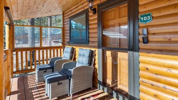 A wooden cabin with a porch featuring wicker furniture and a large window. - Greer Cozy Cottage (Cabin 103) (Greer)