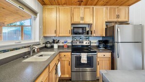 A kitchen with wooden cabinets, stainless steel appliances, a double sink, and a window providing natural light. - Greer Cozy Cottage (Cabin 103) (Greer)