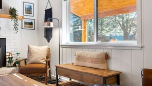 A cozy room with a wooden table, a bench, and a large window with a view of trees. - Greer Cozy Cottage (Cabin 103) (Greer)
