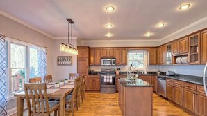 A spacious kitchen with wooden cabinets, a central island, and a dining area with wooden chairs and a table. - Lakehouse, Dock, Hot Tub & Tesla charger. Ideal for entertaining. Pet-Friendly! (Hiawassee)
