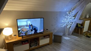 A living room with a television on a wooden stand, a lamp, and a decorative tree with lights. - Loft near Gerardmer (Corcieux)