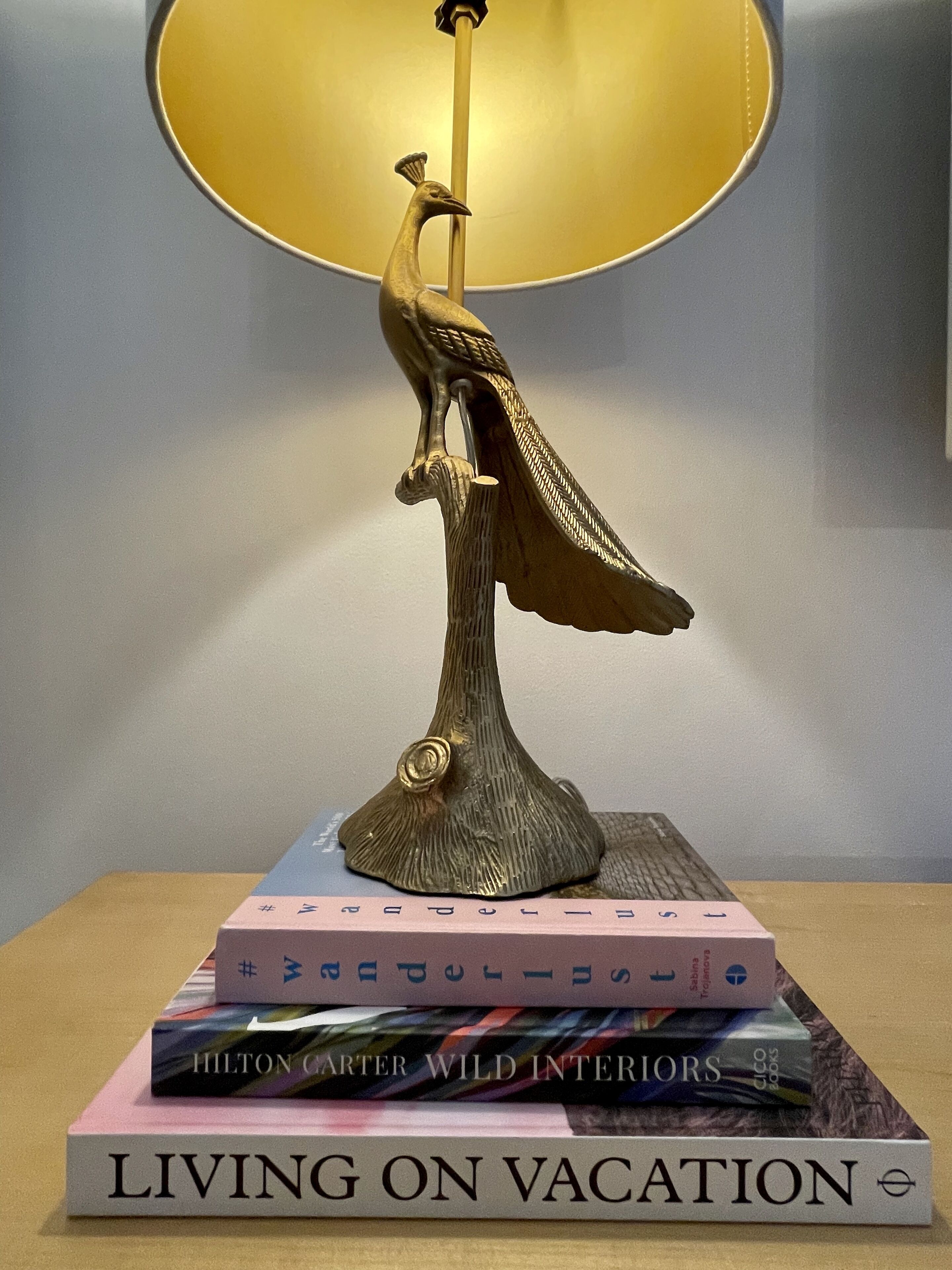 A decorative lamp with a peacock design on a table, surrounded by books.