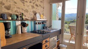 A kitchen with a stone wall, wooden cabinets, and a balcony with a view of the countryside. - Relaxing peaceful retreat for 2 in a rural village in the Pyrenees (Rabouillet)