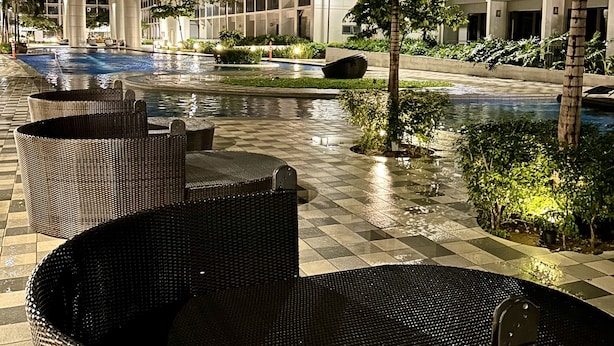 Ein Hotelinnenhof mit Swimmingpool, Sitzgelegenheiten im Freien und einem hohen Gebäude im Hintergrund.