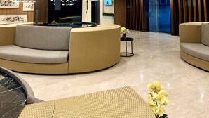 Eine moderne Lobby mit hohen Decken, hängenden Pendelleuchten und einer zentralen Sitzgruppe mit Sofas.