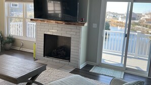 A living room with a fireplace, a flat-screen TV, a large window, and a balcony. - Beautiful home in quiet beach neighborhood on canal. Five minute walk to beach. (Virginia Beach)