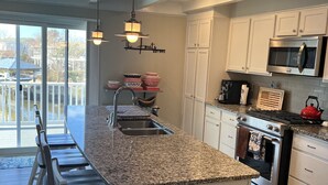 A modern kitchen with a granite countertop, stainless steel appliances, and a dining area with bar stools. - Beautiful home in quiet beach neighborhood on canal. Five minute walk to beach. (Virginia Beach)