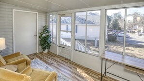 A sunroom with a wooden floor, a yellow sofa, a potted plant, and large windows overlooking a street. - Family friendly home near Colonial Williamsburg and Busch  Gardens (Williamsburg)