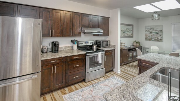 A modern kitchen with dark wooden cabinets, stainless steel appliances, granite countertops, and a central island with a sink. - Family friendly home near Colonial Williamsburg and Busch  Gardens (Williamsburg)