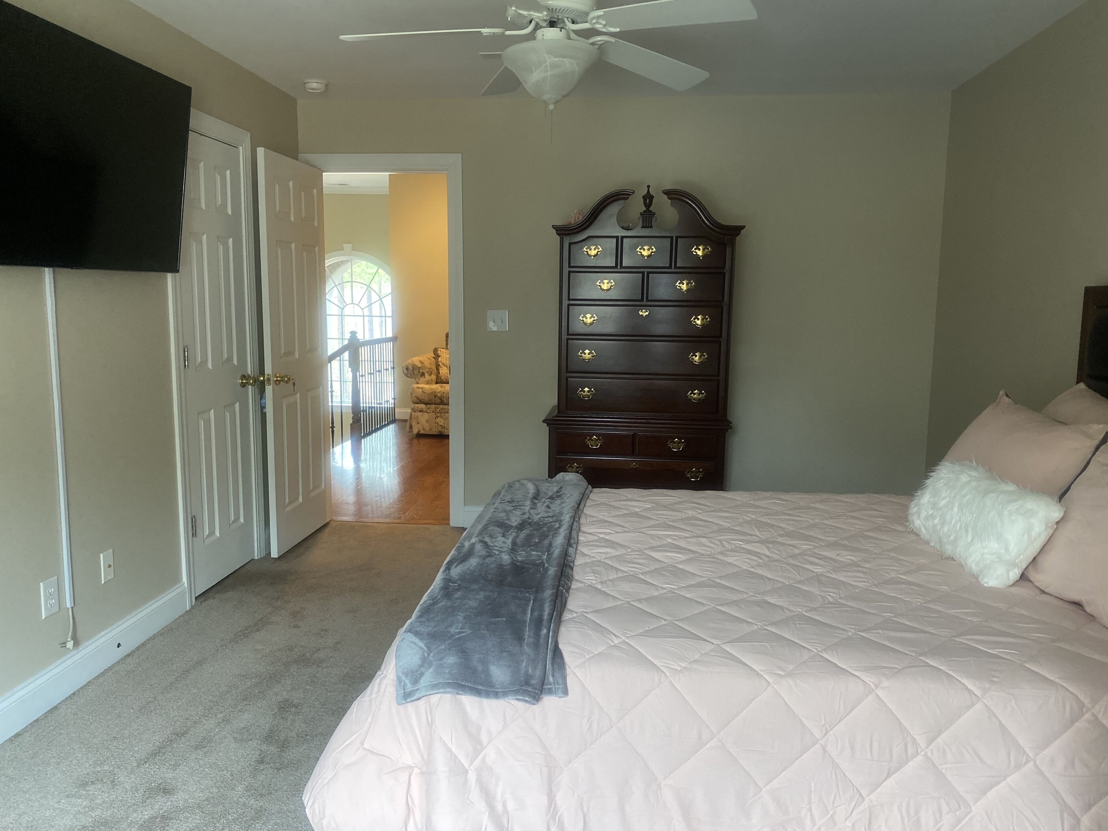A bedroom with a bed, a dresser, a ceiling fan, and a TV on the wall.