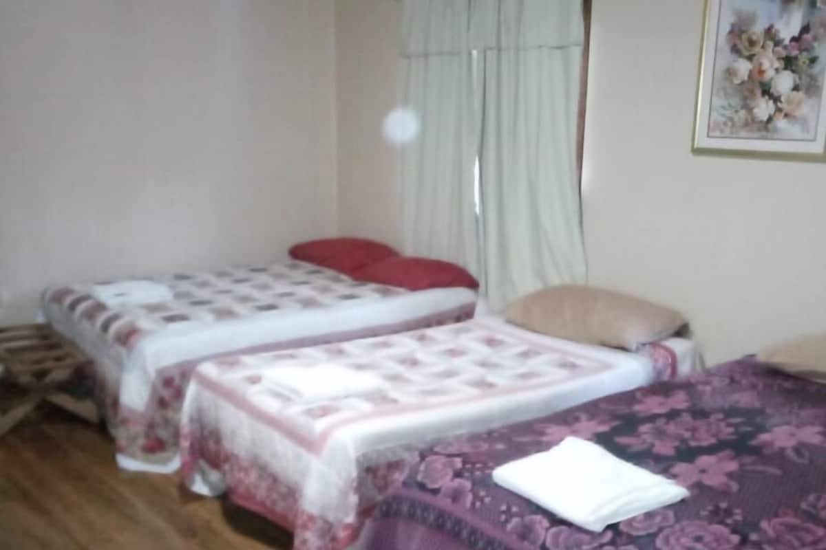A room with two single beds, a wooden floor, a window with curtains, and a framed picture on the wall.
