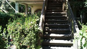 A wooden staircase leading to a wooden house with a balcony. - Casa del campo (Tela)