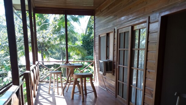 A wooden deck with a table and chairs, large windows, and a view of greenery. - Casa del campo (Tela)