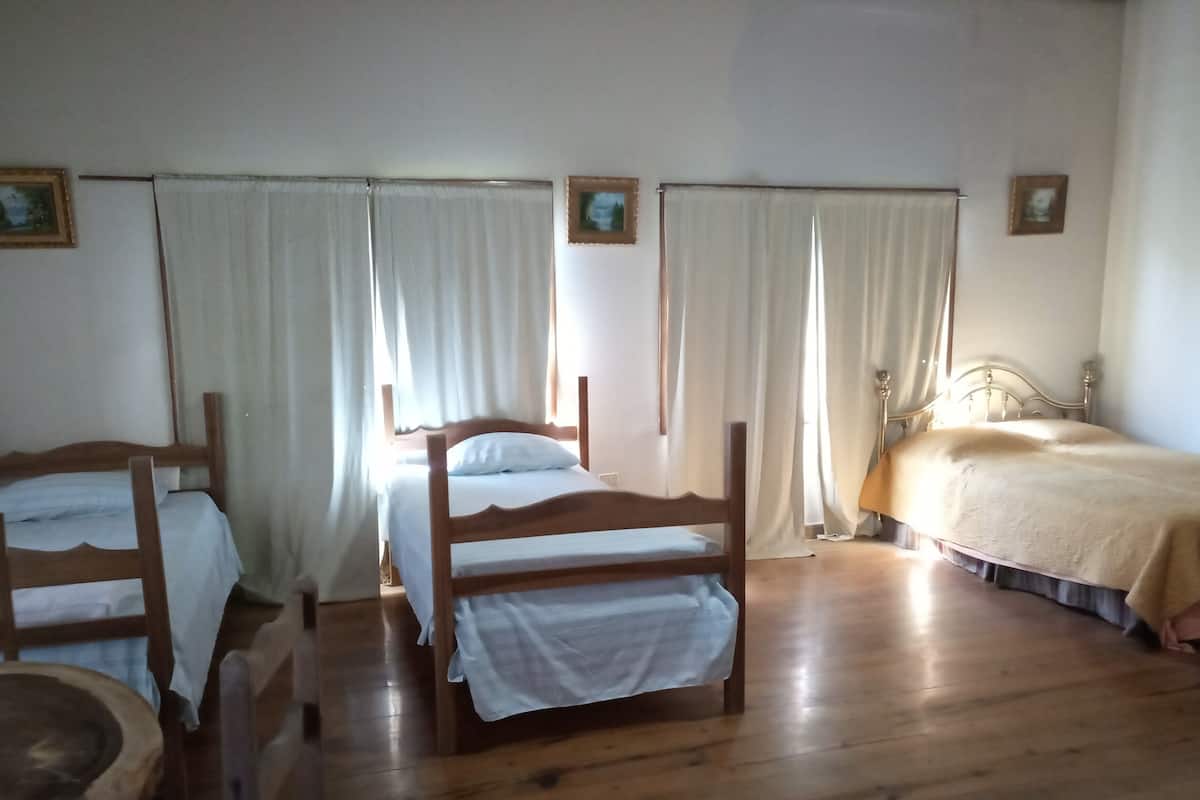 A room with three wooden beds, white curtains, and a wooden floor.