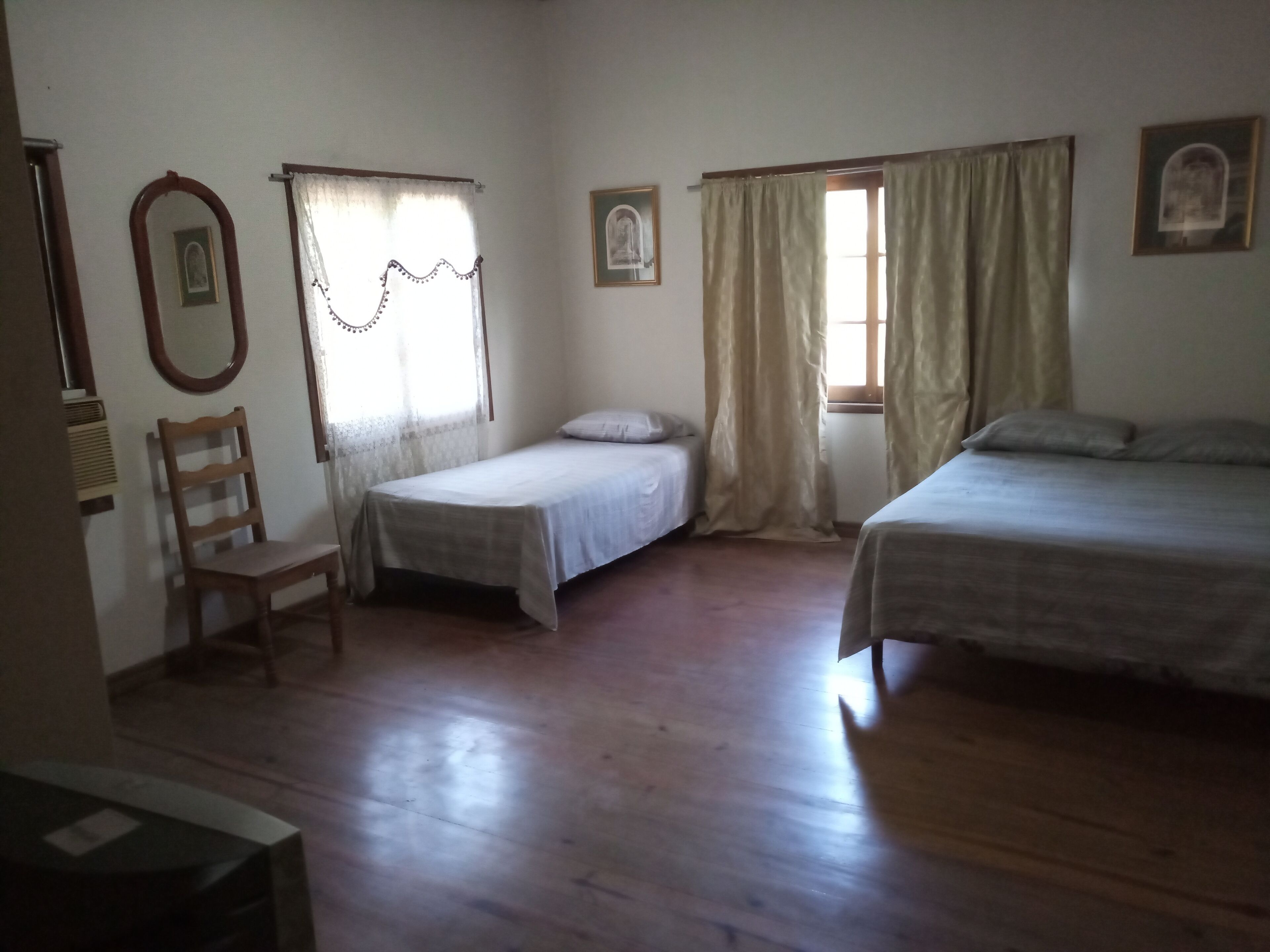 A room with two single beds, a wooden chair, a small table, and a window with curtains.