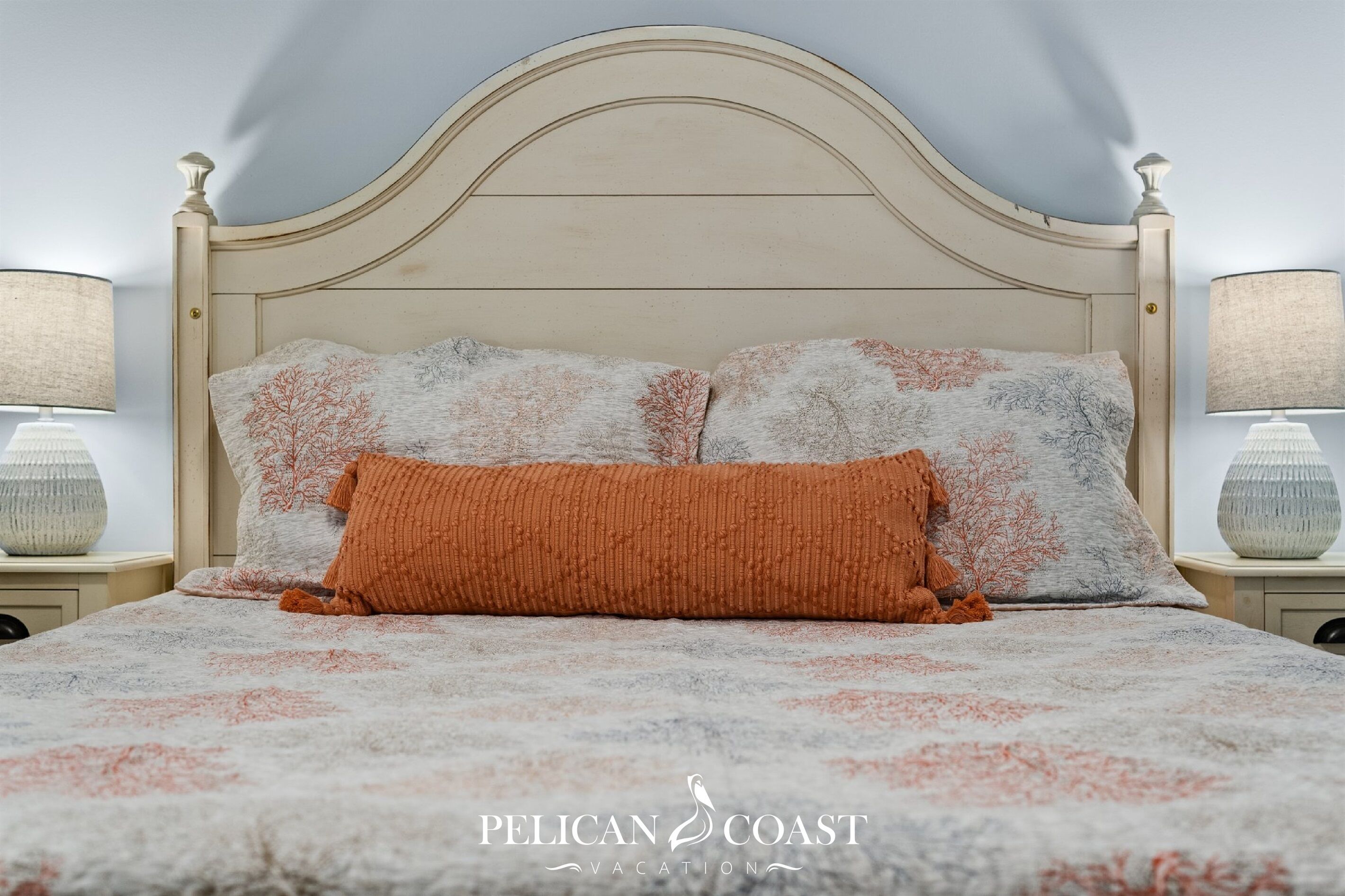 A bed with a patterned bedspread, two pillows, and a nightstand with a lamp.