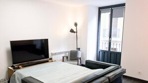A hotel room with a bed, a TV, a bedside table, a lamp, and a window with a view of the outside. - Navarro Suite Pamplona - Family Management (Pamplona)