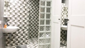 A bathroom with a geometric patterned wall, a glass shower enclosure, and a white sink. - Navarro Suite Pamplona - Family Management (Pamplona)