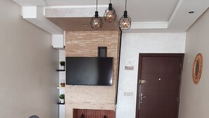 Una sala de estar moderna con una mesa de comedor de cristal, sillas oscuras, un televisor de pantalla plana montado en una pared de madera y una puerta de madera oscura.