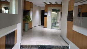 Un pasillo moderno con suelo de mármol, detalles de madera y un ascensor de vidrio.